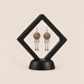 Amber Floraison earrings displayed inside a clear membrane in a black square frame set diagonally on a black base.
