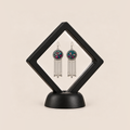 Pastel Refrain pair displayed in a black square clear-membrane frame on a black stand, with the pastel embroidered fronts facing forward.