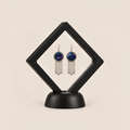 Violet Undertow pair displayed in a black square clear-membrane frame on a black stand, with both blue-violet embroidered fronts facing forward.