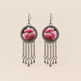 Blush Rhapsody earrings with pink embroidered petals and gold-colored stitched edges on dark round fronts, each with five chain tassels and teardrop ends.