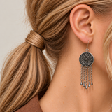 Model with a low side ponytail wearing Garnet Serenade with the round floral metal reverse facing outward above five chain tassels with teardrop ends.