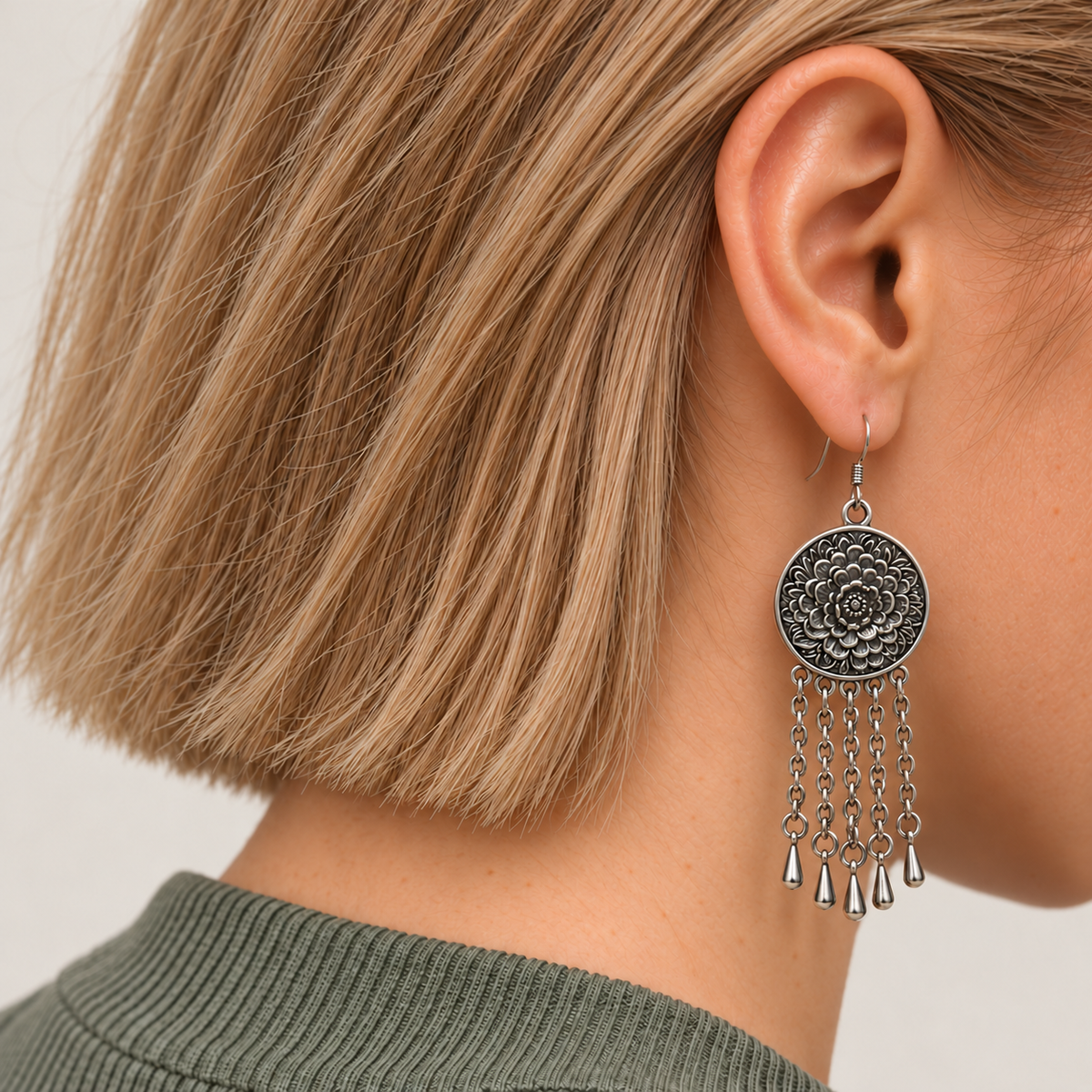 Model with a short bob wearing Coral Reverie with the round floral metal reverse facing outward above five oval-link chains with teardrop pendants.