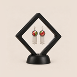 Coral Reverie pair displayed in a black square clear-membrane frame on a black stand, with both red-and-green embroidered fronts facing forward.