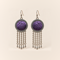 Violet Cadence earrings with purple counted-thread embroidery and dark angular outlines in round patterned frames, each with five oval-link chains and teardrop pendants.