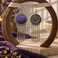 Violet Cadence earrings hanging through holes in a pale textured strap across a round wooden arch, showing the purple embroidered front and floral reverse.