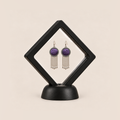 Violet Cadence pair displayed in a black square clear-membrane frame on a black stand, with both purple geometric embroidered fronts facing forward.
