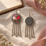 Petal Dialogue earrings on cream woven cloth beside an open notebook and pink ribbon, showing one embroidered front and one floral reverse with three drops and two spheres each.