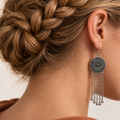 Model with a braided crown wearing Crimson Confluence with the round floral metal reverse facing outward above five long oval-link chains with teardrop ends.