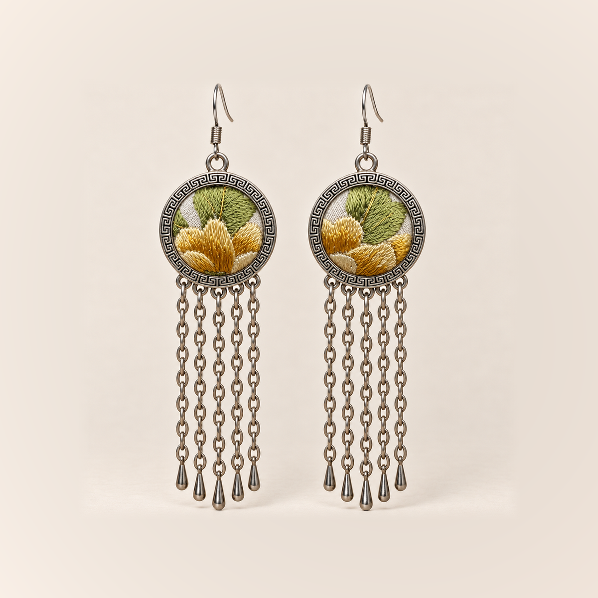 Golden Solace earrings with golden-yellow embroidered petals and light green leaves on pale round fronts, each with five long oval-link chains and teardrop ends.
