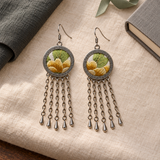 Golden Solace pair on cream woven cloth beside dark fabric, a gray book and green ribbon, with both yellow-and-green embroidered fronts facing up.