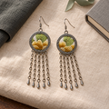 Golden Solace pair on cream woven cloth beside dark fabric, a gray book and green ribbon, with both yellow-and-green embroidered fronts facing up.