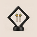 Golden Solace pair displayed in a black square clear-membrane frame on a black stand, with both yellow-and-green embroidered fronts facing forward.