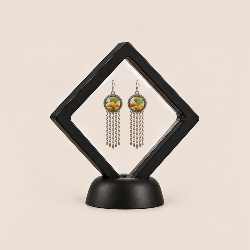 Golden Solace pair displayed in a black square clear-membrane frame on a black stand, with both yellow-and-green embroidered fronts facing forward.