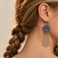 Model looking downward while wearing the floral metal reverse of a Scarlet Affinity earring with five long chains and teardrop pendants.
