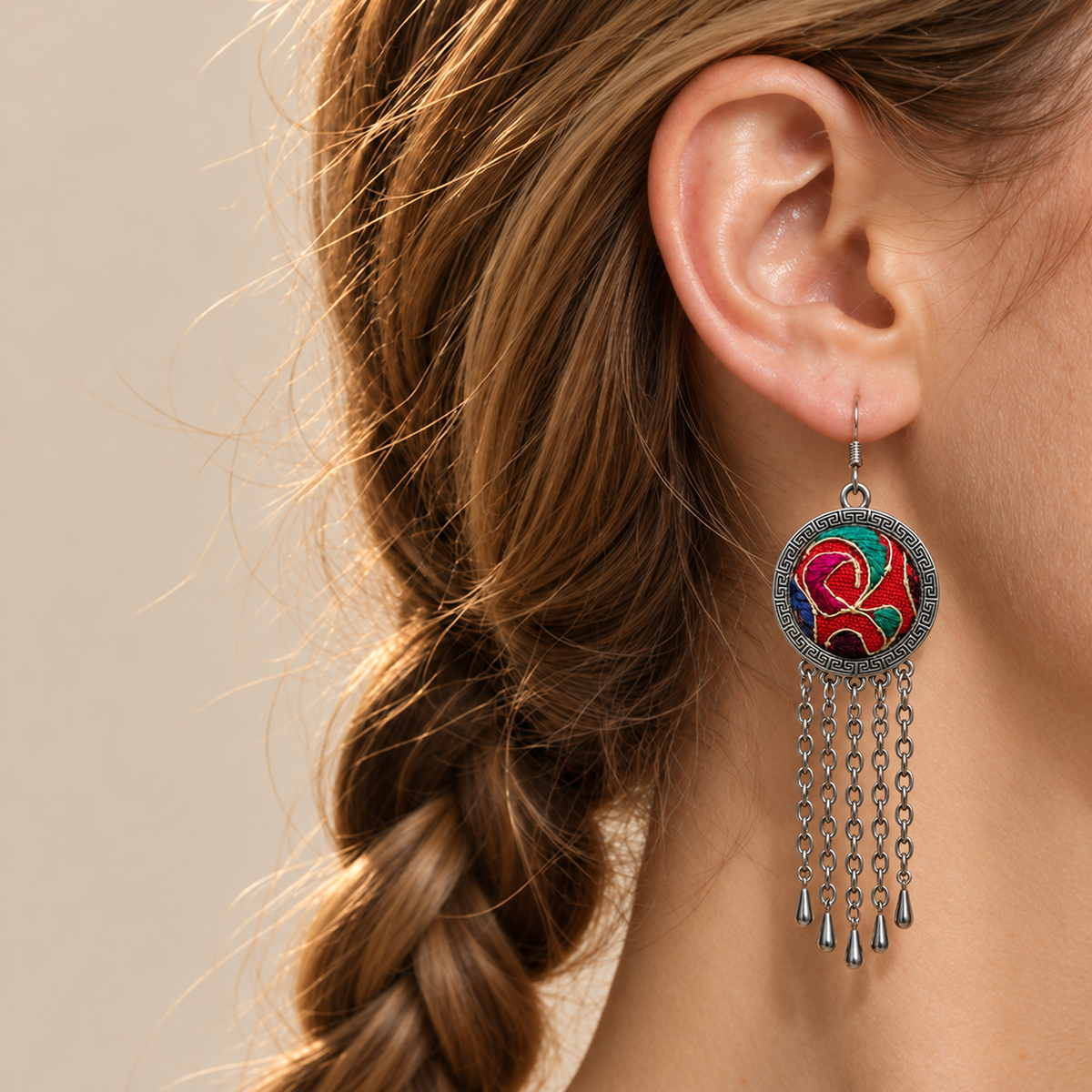 Scarlet Affinity earring worn at the ear, showing red, teal and magenta embroidery with pale curving outlines and five long chain tassels.