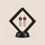 Scarlet Affinity earrings displayed in a tilted black square membrane frame on a round black base.