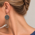 Model looking downward while wearing the floral metal reverse of an Ember Refrain earring with five long chains and teardrop pendants.