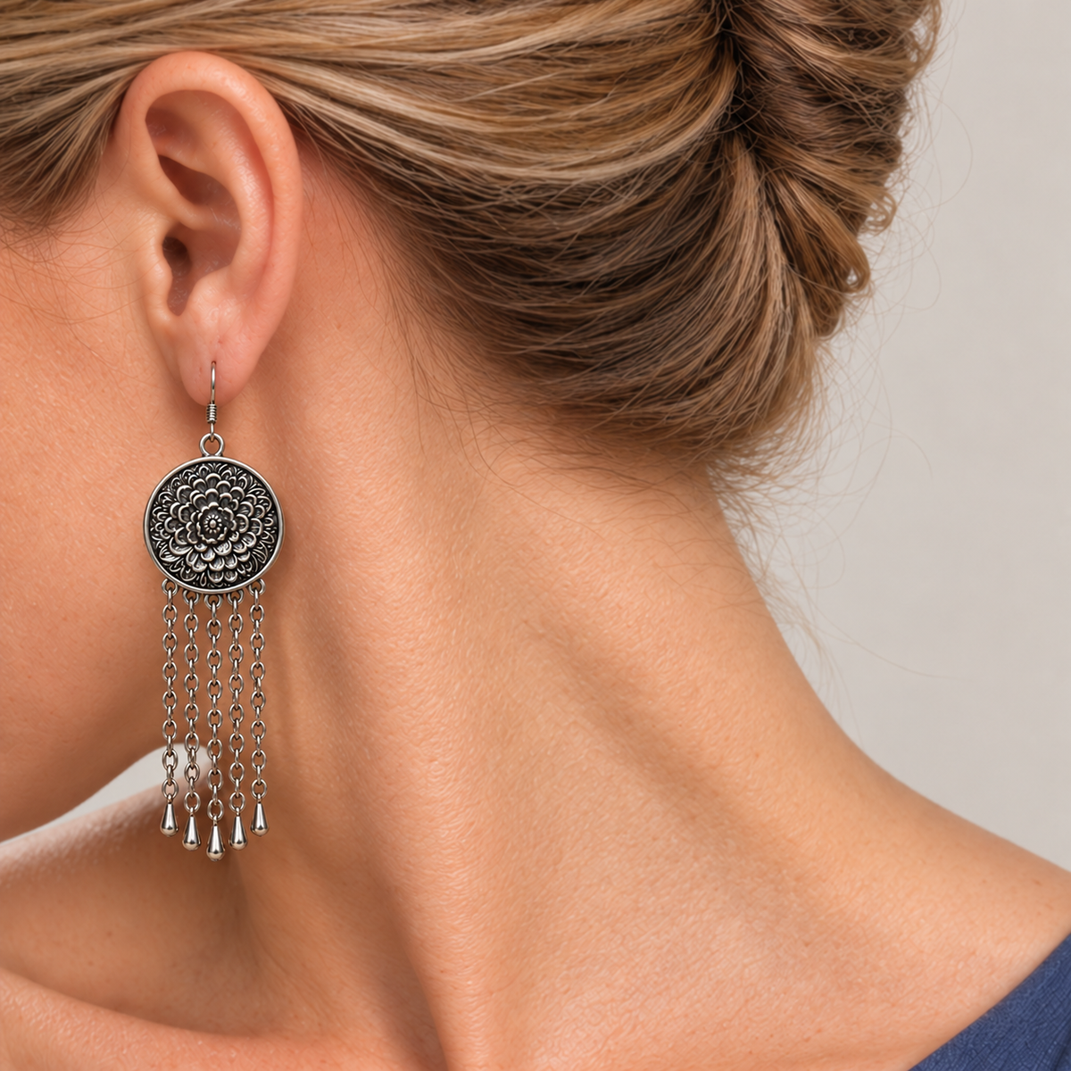 Model looking downward while wearing the floral metal reverse of an Ember Refrain earring with five long chains and teardrop pendants.