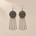 Pair of Ember Refrain floral metal reverses on cream cloth, with smooth outer rims and five long oval-link chains ending in teardrops.