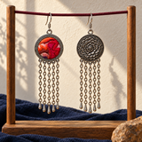 Ember Refrain embroidered front and floral reverse hanging from a burgundy cord between wooden posts, above blue fabric with a stone beside the stand.