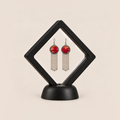 Ember Refrain earrings displayed in a tilted black square membrane frame on a round black base.