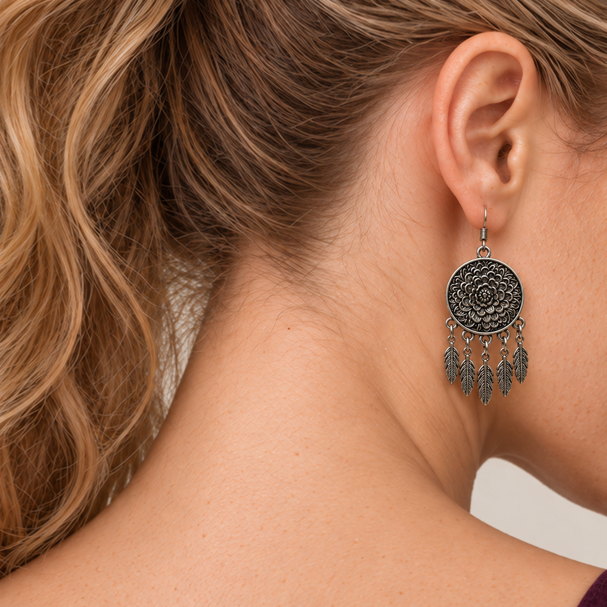 Model looking downward while wearing the floral metal reverse of a Garden Murmur earring with five flat leaf pendants on short chains.