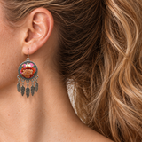 Garden Murmur earring worn at the ear, showing warm floral embroidery on pink and mint, a patterned circular rim and five flat leaf pendants.