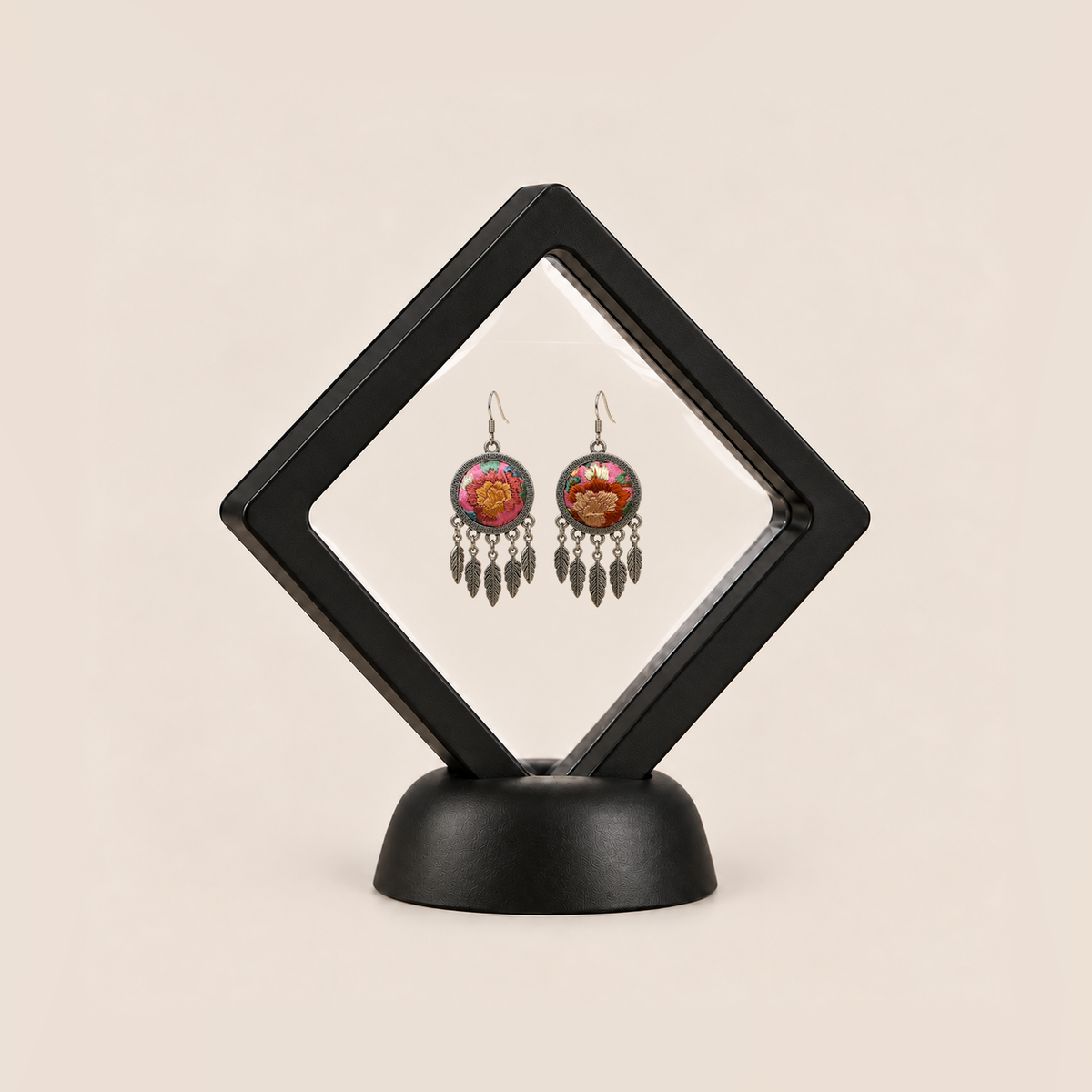 Garden Murmur leaf earrings displayed in a tilted black square membrane frame on a round black base.