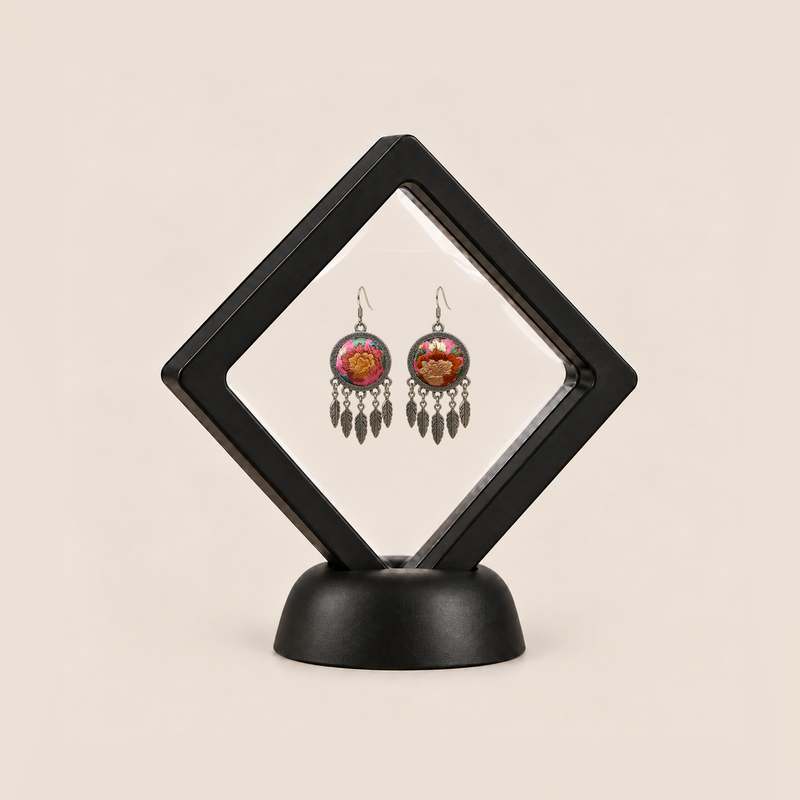 Garden Murmur leaf earrings displayed in a tilted black square membrane frame on a round black base.