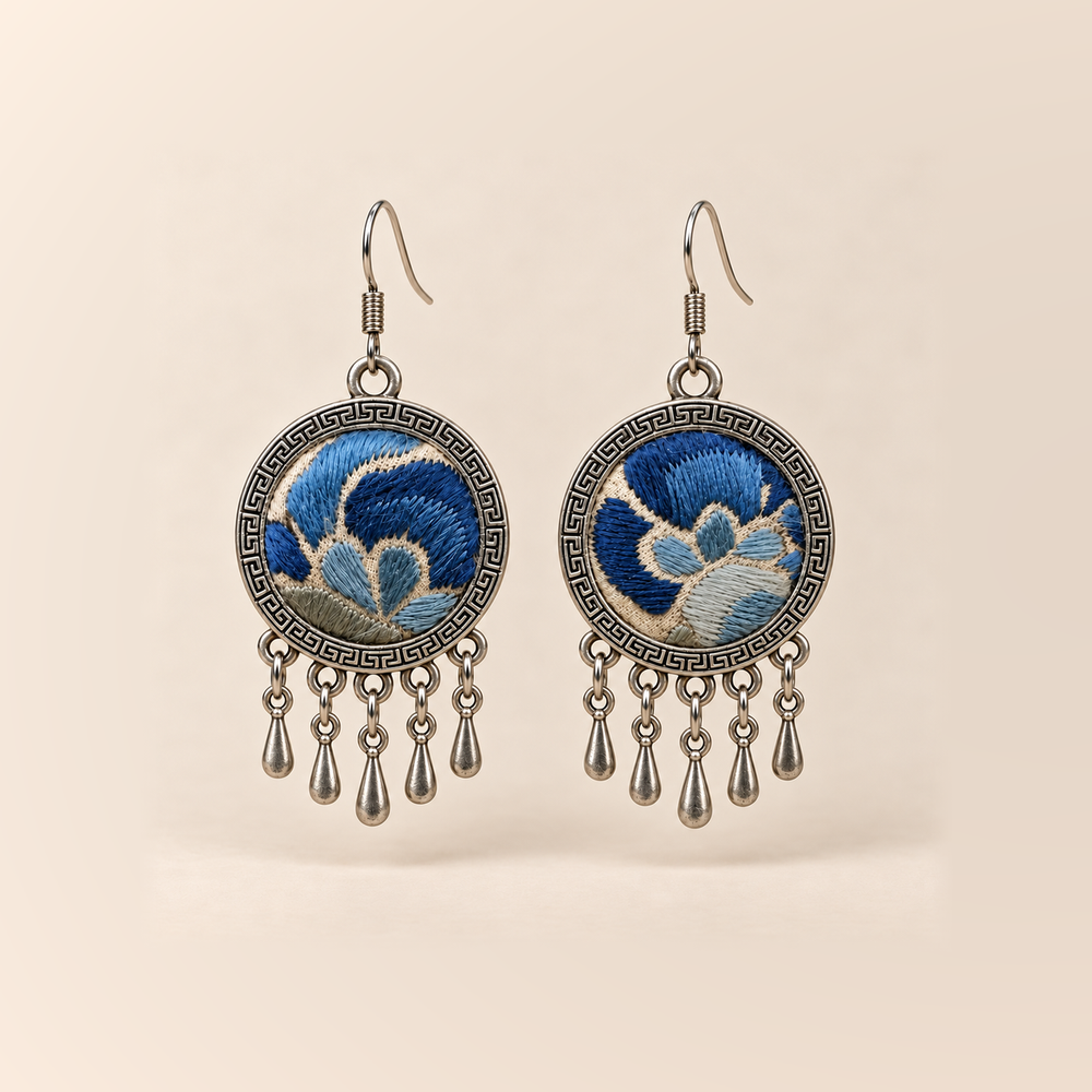 Azure Harmony Three-Blue Embroidery earrings with deep and pale blue floral curves on ivory-colored cloth, patterned rims and five short teardrop pendants.