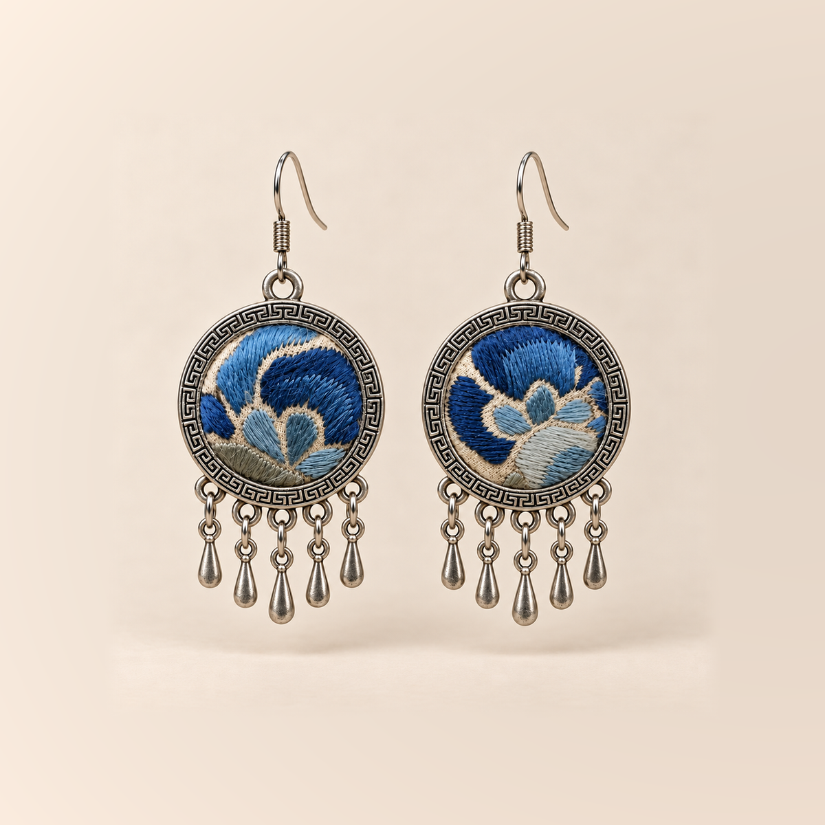 Azure Harmony Three-Blue Embroidery earrings with deep and pale blue floral curves on ivory-colored cloth, patterned rims and five short teardrop pendants.