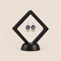 Azure Harmony drop earrings displayed in a tilted black square membrane frame on a round black base.