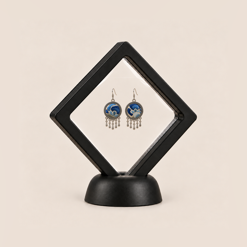 Azure Harmony drop earrings displayed in a tilted black square membrane frame on a round black base.