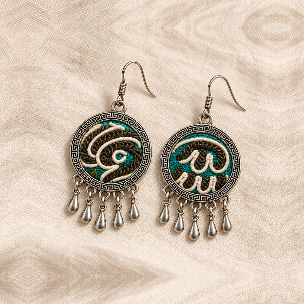 Both Teal Reverie embroidered fronts face upward on cream woven cloth, showing their distinct pale curving outlines and five short teardrops each.