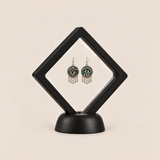 Teal Reverie drop earrings displayed in a tilted black square membrane frame on a round black base.