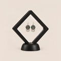 Teal Reverie drop earrings displayed in a tilted black square membrane frame on a round black base.