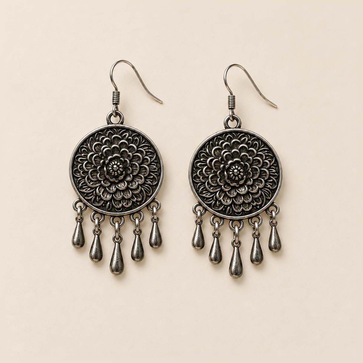Pair of Chromatic Accord floral metal reverses on cream cloth, each with a smooth outer rim and five short teardrop pendants.